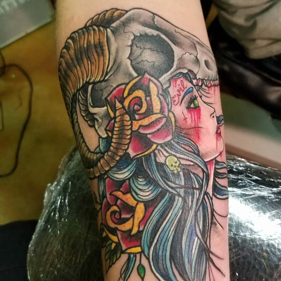 A color neo traditional woman wears a horned skull headdress on a forearm.