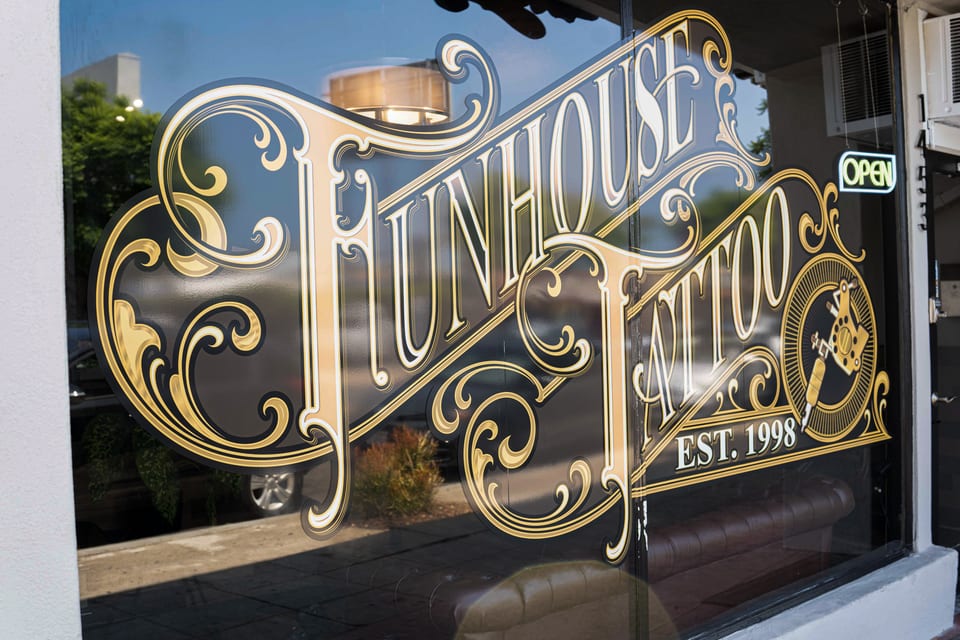 Gold Funhouse Tattoo lettering fills the shop window beside a lit open sign.