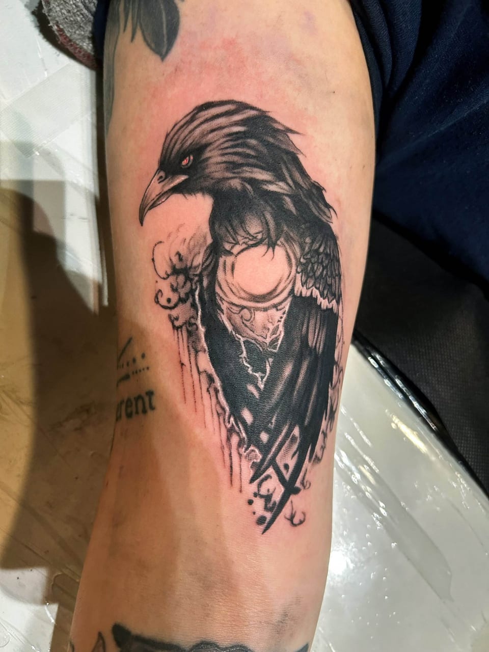 A black illustrative raven cradles a glowing orb on the upper arm.