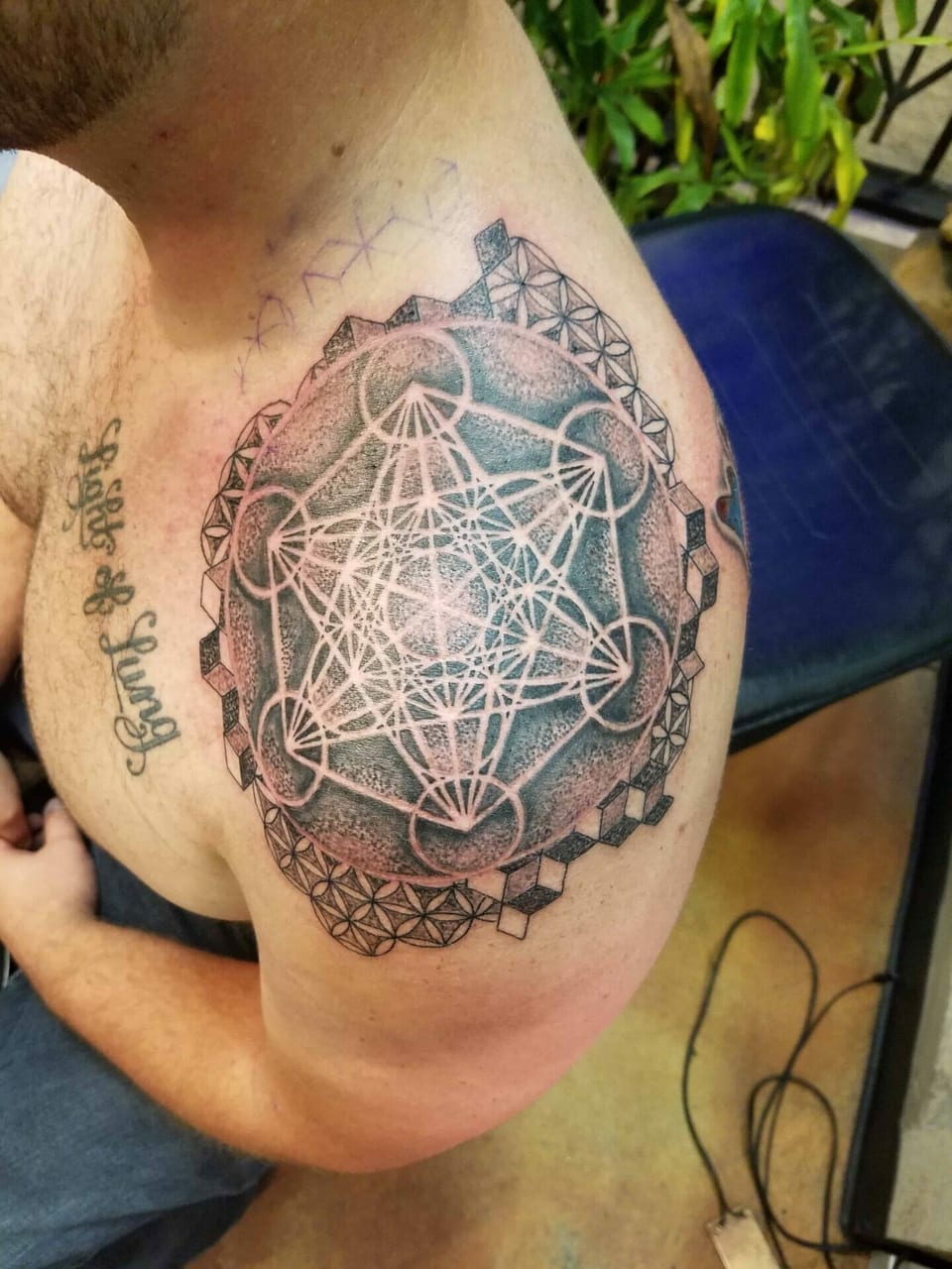 A black geometric circle with intersecting lines and cube borders covers a shoulder.