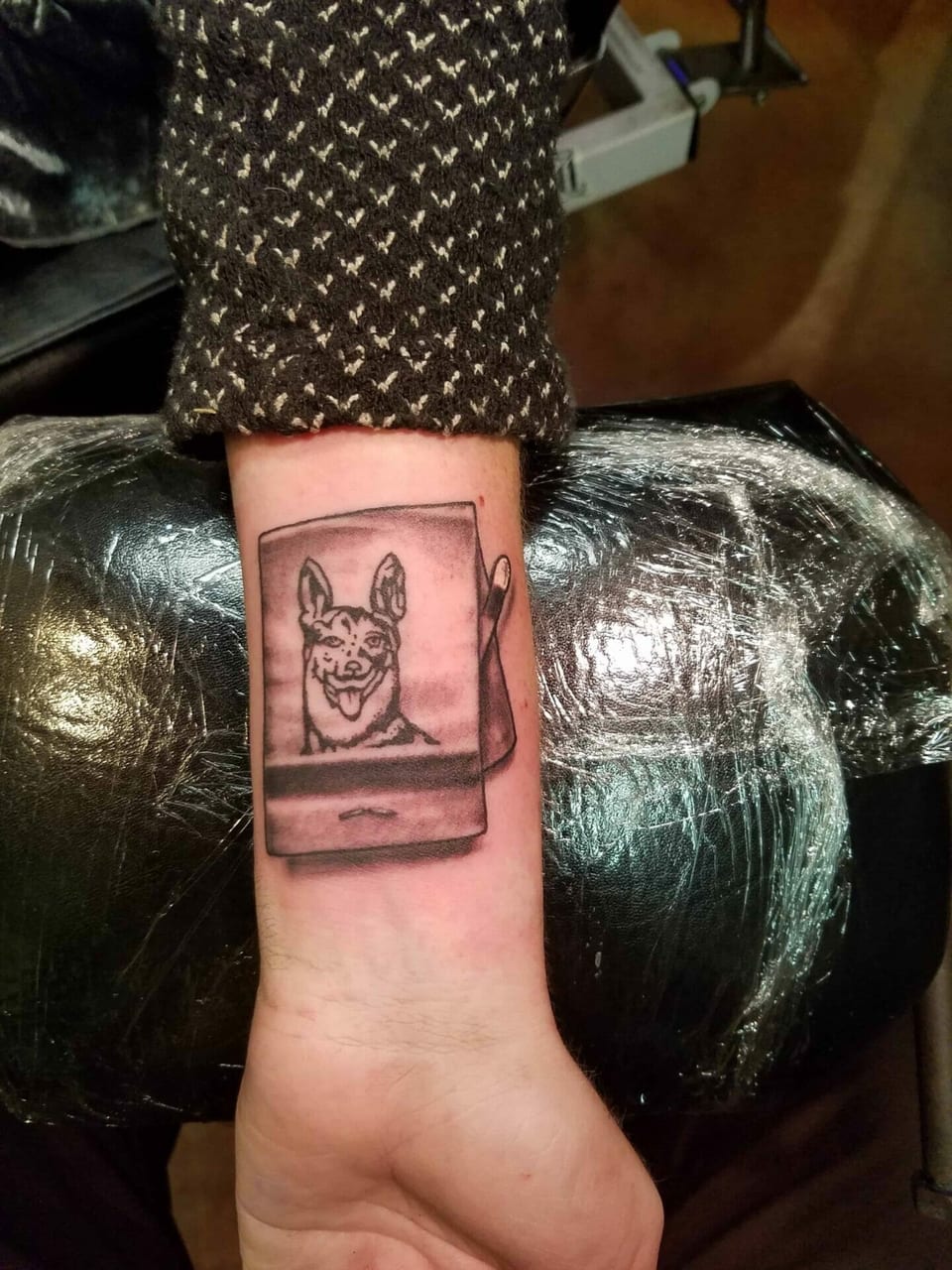 A black and grey illustrative dog portrait fills a matchbook tattoo on a wrist.