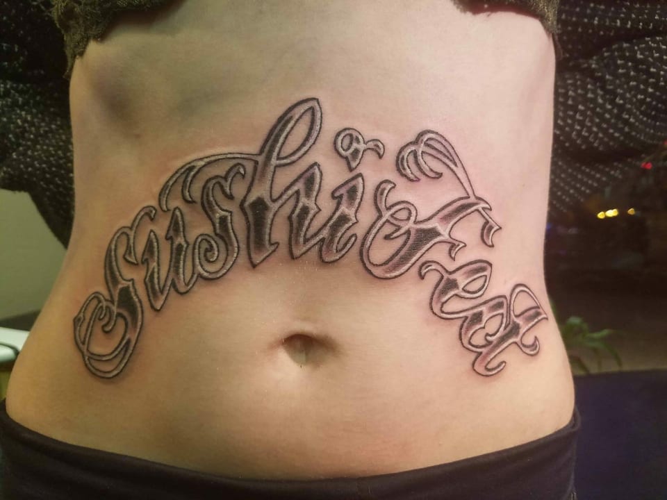 Black and grey script arches across the abdomen above the navel.