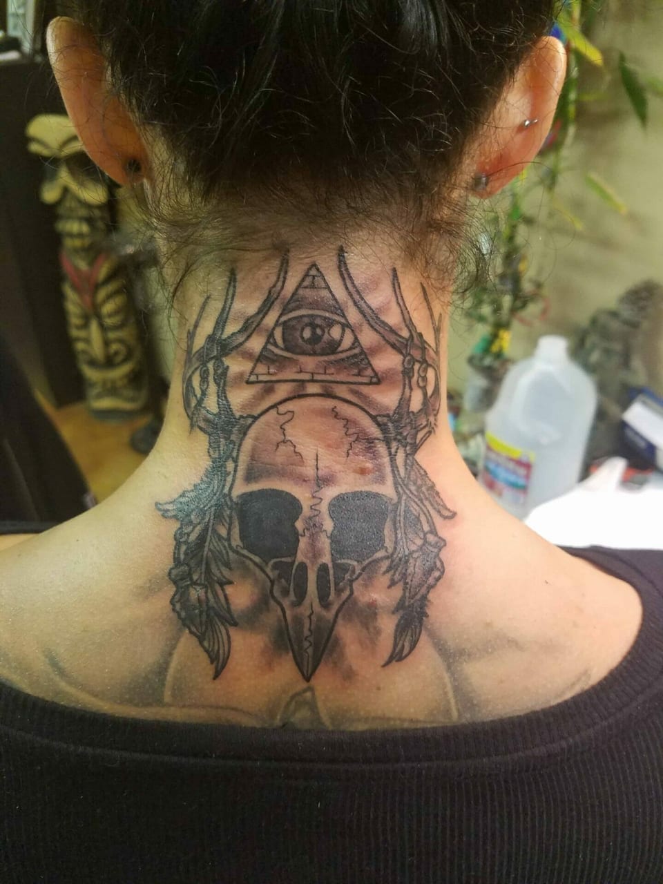 A black and grey illustrative skull and antlers sit beneath a triangular eye on the neck and upper back.