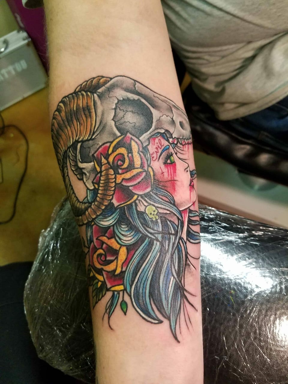 A color neo traditional woman wears a horned skull headdress on a forearm.
