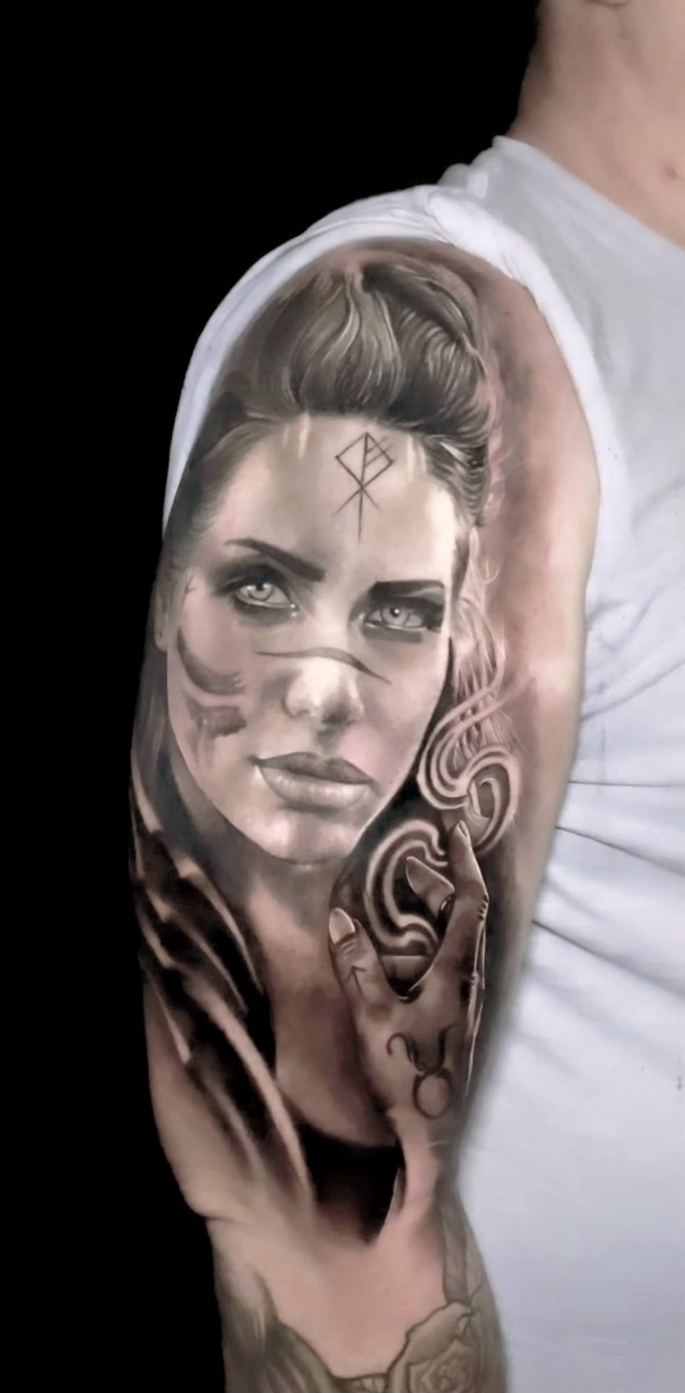 A black and grey realism woman with forehead markings and flowing hair covers an upper arm.
