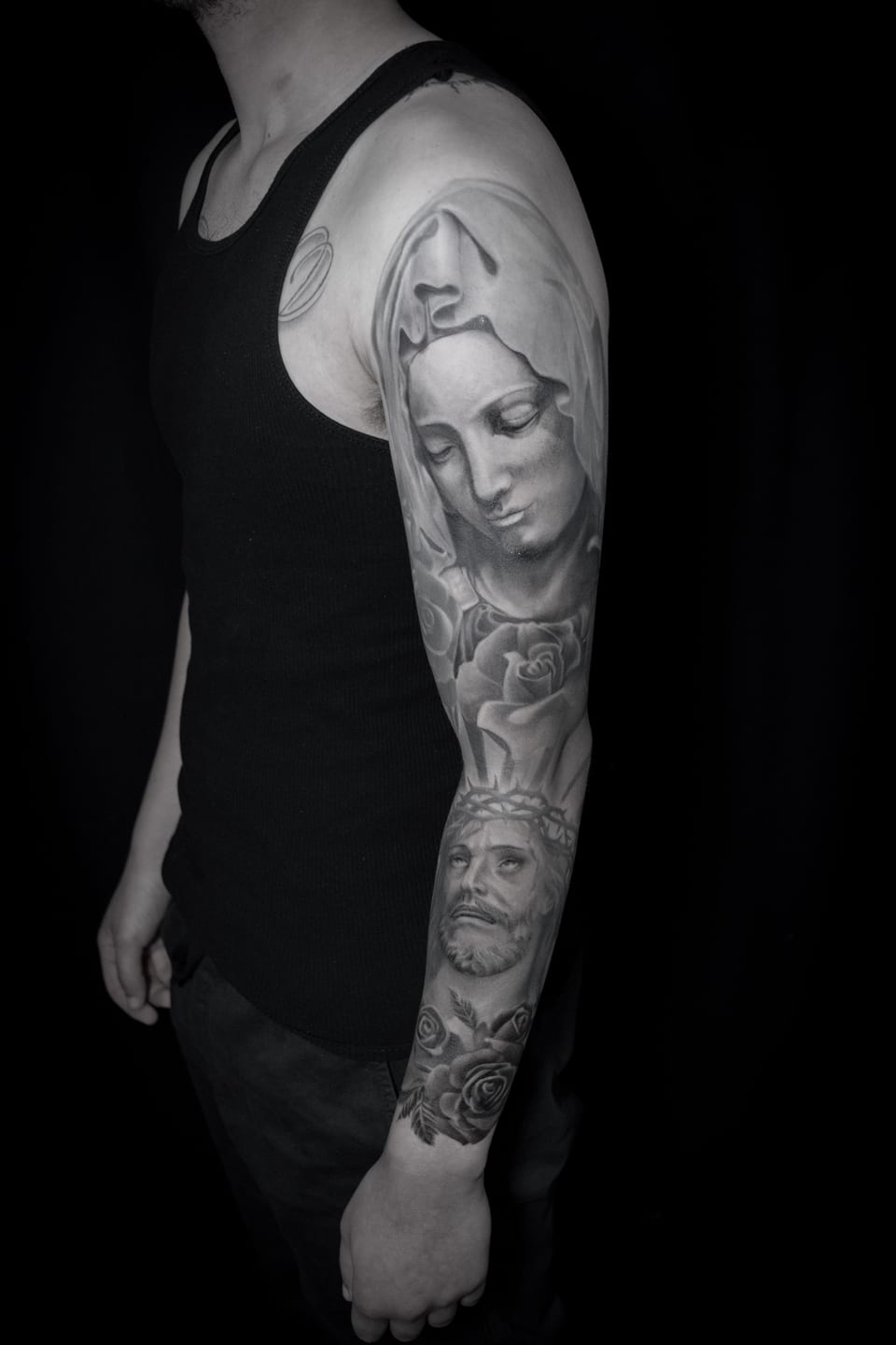 A black and grey realism sleeve combines a veiled woman, thorn-crowned man and roses.