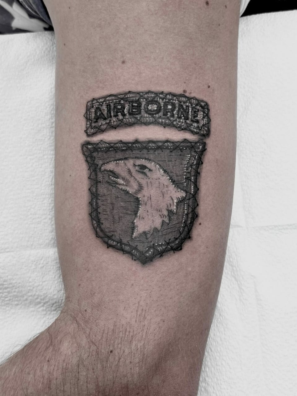 A black and grey realism embroidered airborne eagle patch covers an inner upper arm.