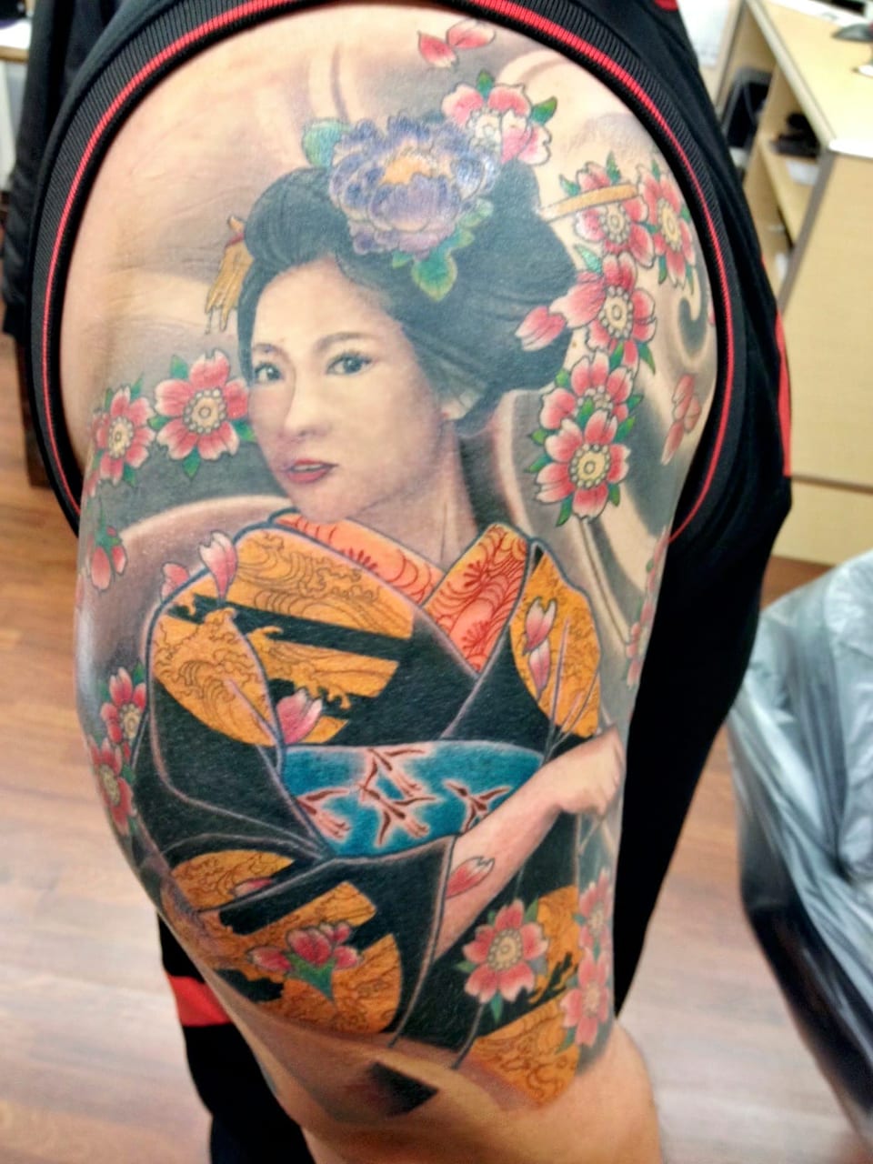 A color Japanese woman in a patterned kimono among pink blossoms covers an upper arm.