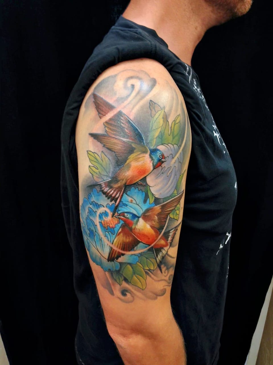 Color illustrative swallows and blue flowers cover an upper arm.