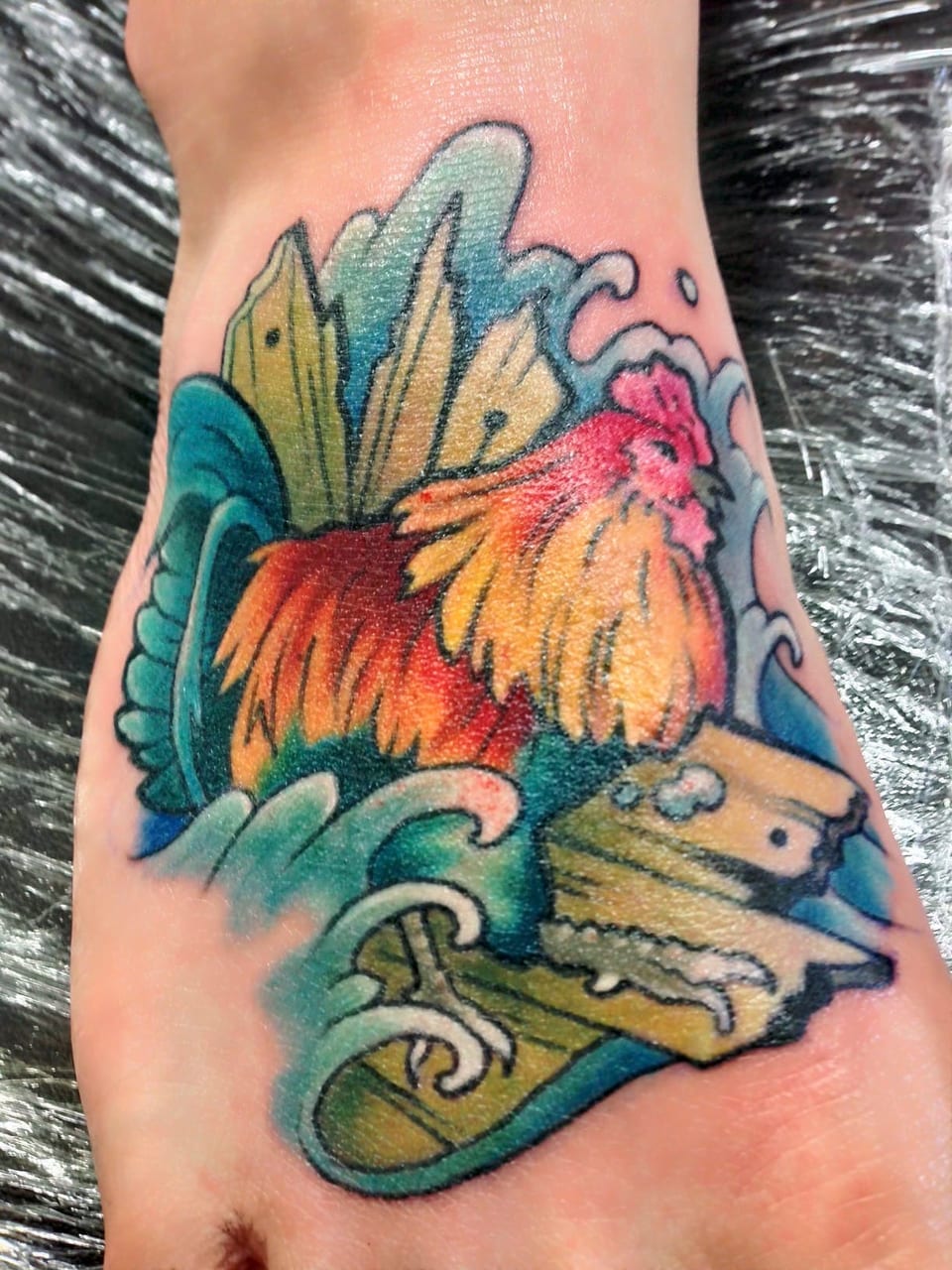 A color illustrative rooster among blue waves and broken wooden planks covers the top of a foot.