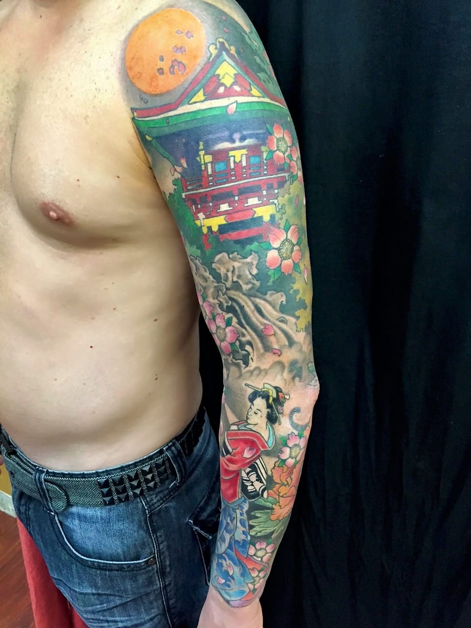 A color Japanese sleeve combines a temple, orange moon, woman and blossoms.