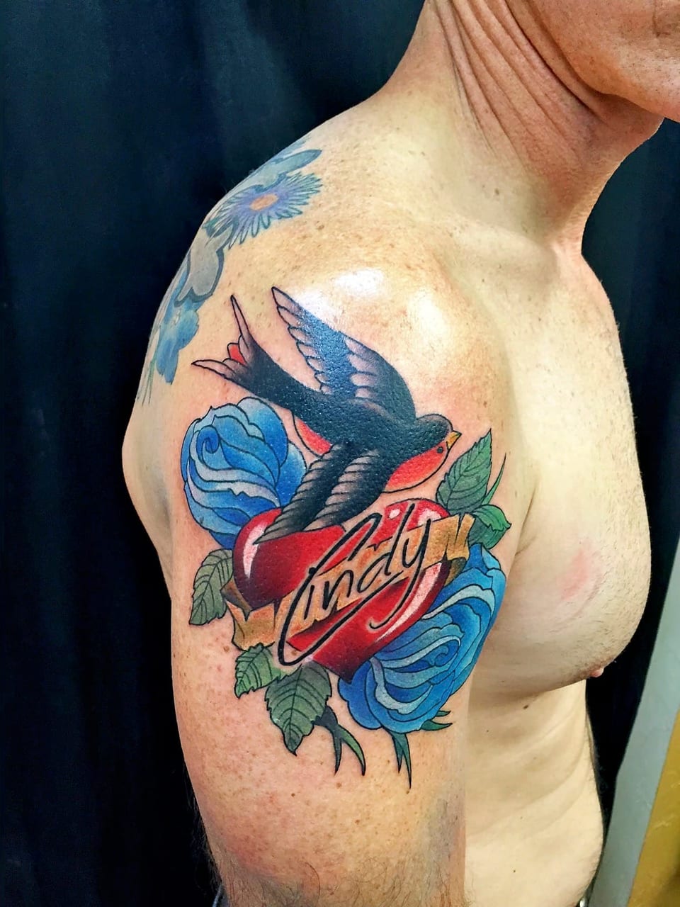 A color traditional swallow, red heart and blue roses cover an upper arm.