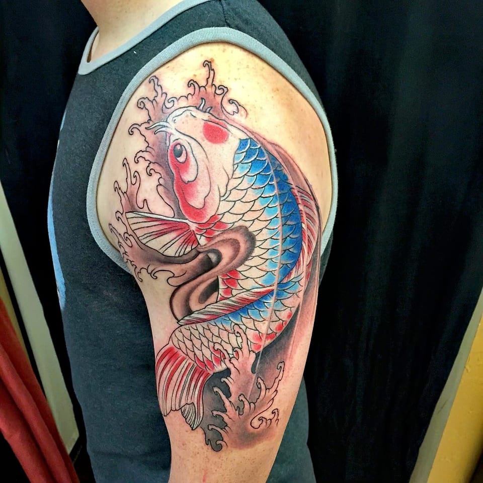 A color Japanese blue, white and red koi swimming through waves covers an upper arm.