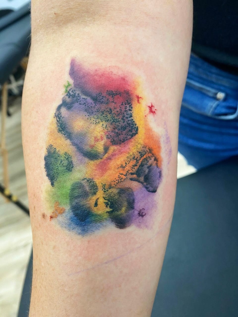 A dark paw print sits against rainbow watercolor splashes on the forearm.
