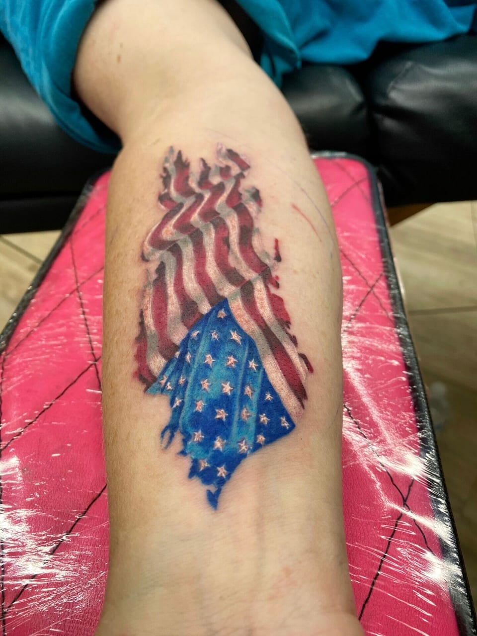 A realistic torn American flag with red stripes and white stars on blue covers the forearm.