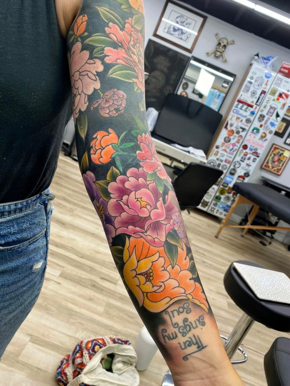 Pink, purple and orange peonies fill a Japanese arm sleeve above script reading 'Then sings my soul' at the wrist.