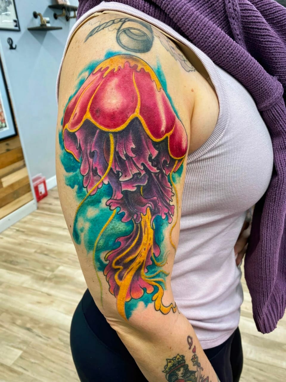 A neo-traditional pink jellyfish trails purple and gold tentacles against turquoise on the upper arm.