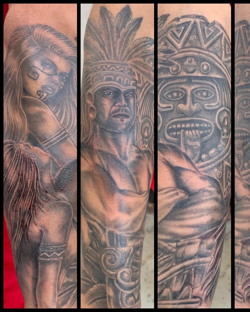 Black and grey realism sleeve tattoo combines figures in feathered headdresses and carved faces in several views.