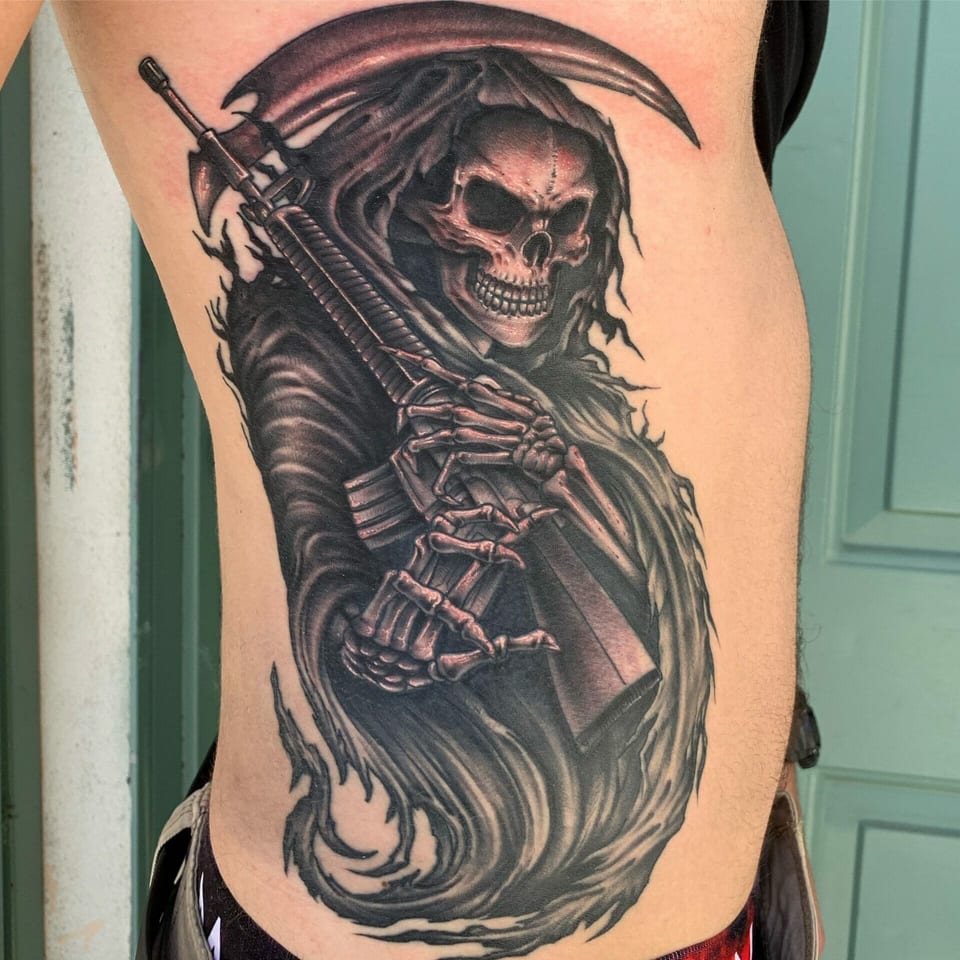Black and grey realism grim reaper with a rifle and scythe covers the ribs.