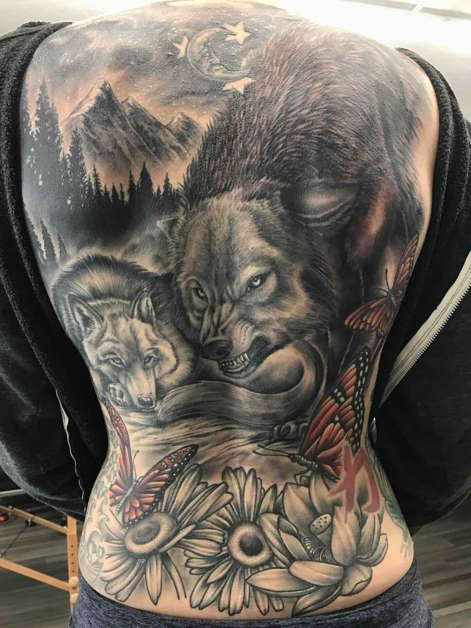 Black and grey realism wolves and a mountain forest cover the back above flowers and orange butterflies.