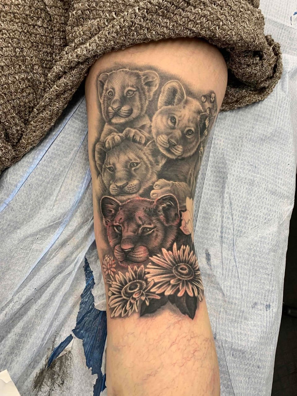 Black and grey realism lion cubs above sunflowers cover the arm.
