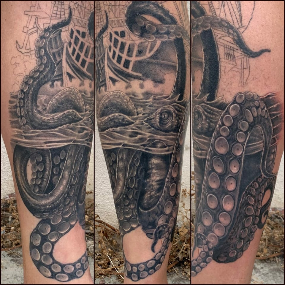 Black and grey realism octopus and sailing ship wrap around the lower leg in several views.