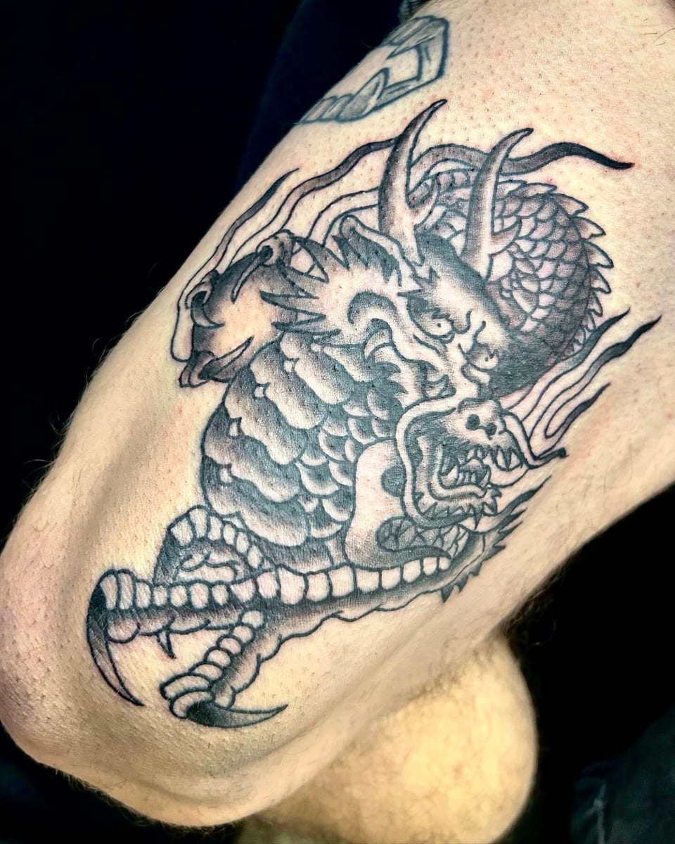 Black and grey traditional coiled dragon with claws sits on the thigh.
