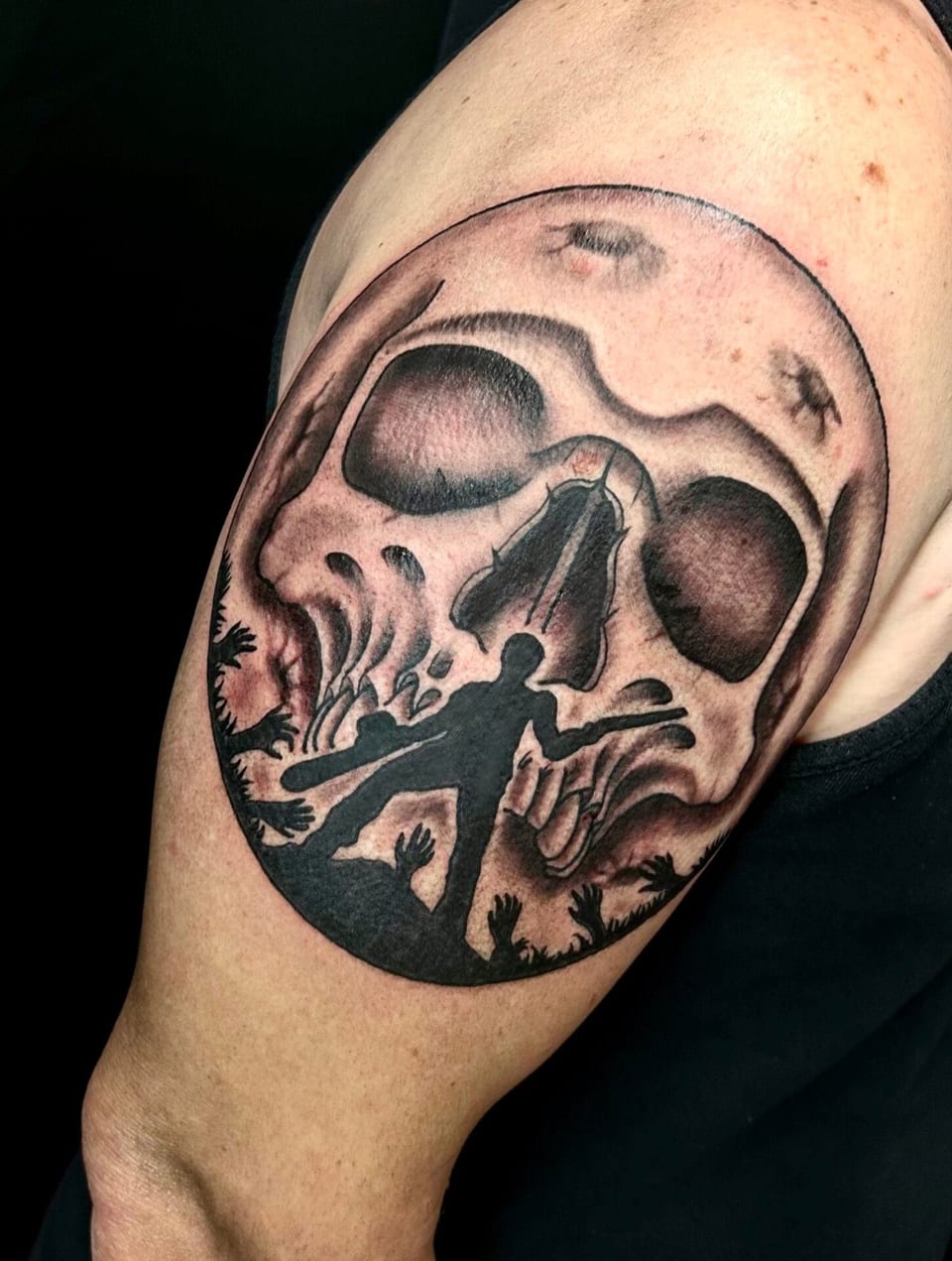 Black and grey illustrative skull frames silhouettes of figures on the upper arm.