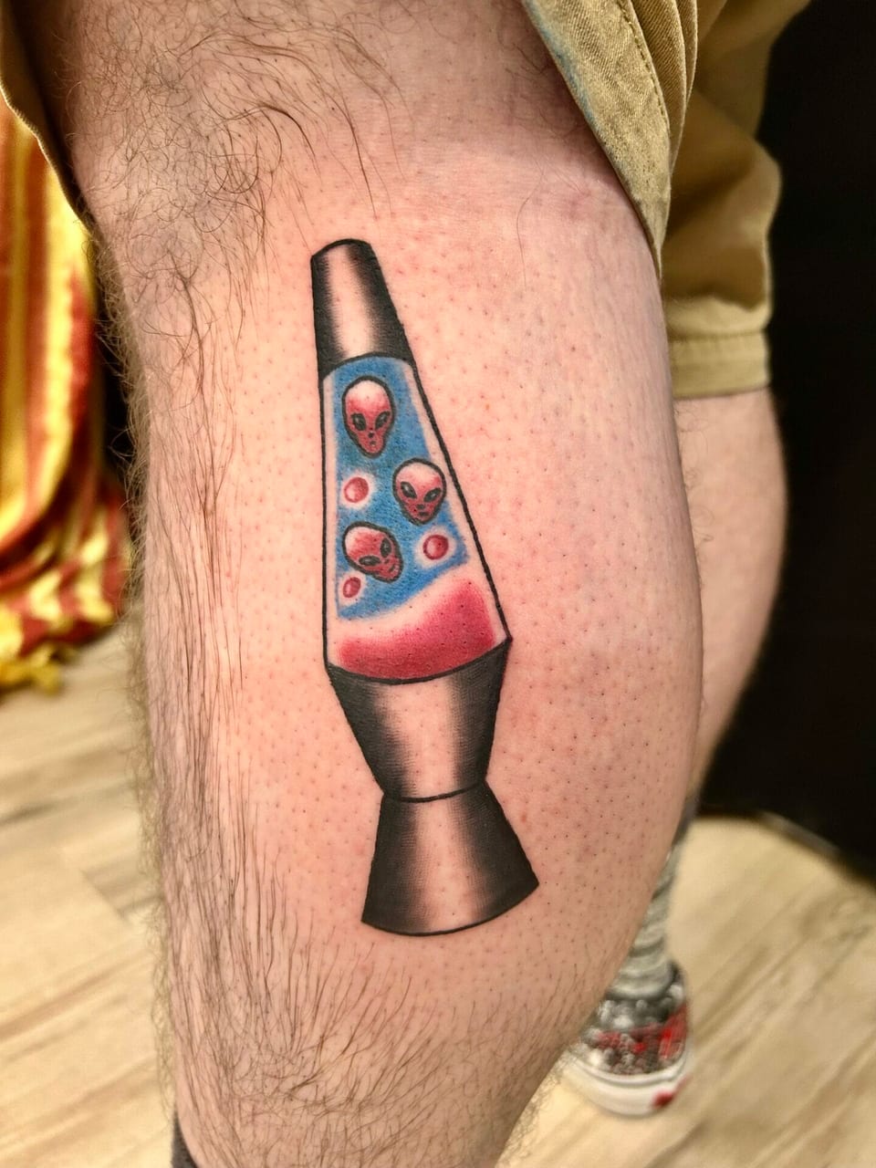 A colorful illustrative lava lamp holds red alien faces in blue liquid on a closely cropped leg.
