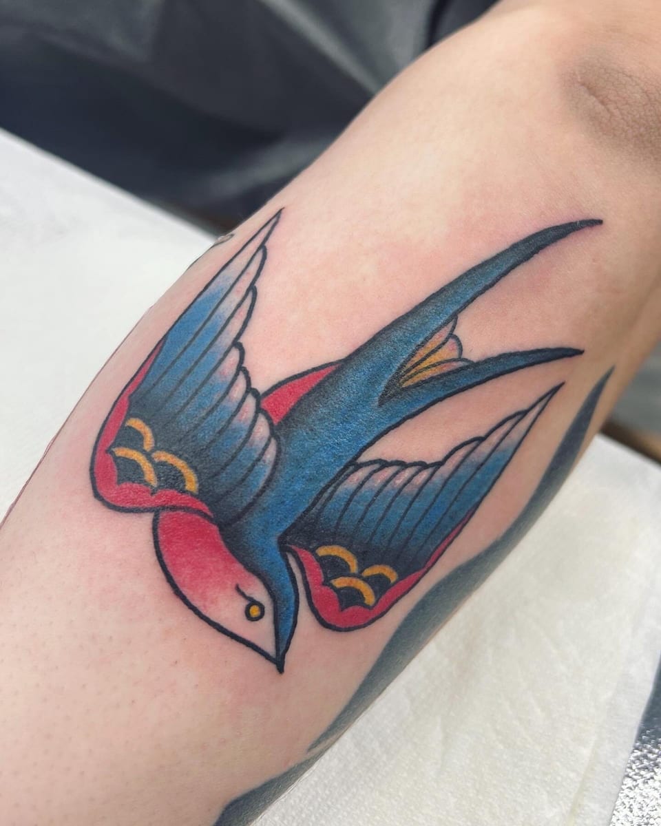 Traditional color swallow with blue wings and red accents sits on the forearm.