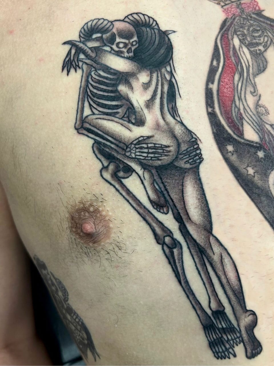 Black and grey illustrative skeleton embracing a woman covers the chest.