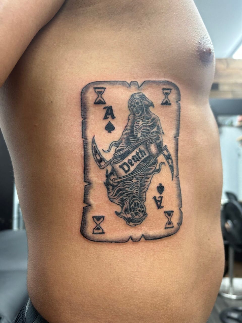 Black and grey illustrative ace of spades with a grim reaper and a Death banner sits on the ribs.
