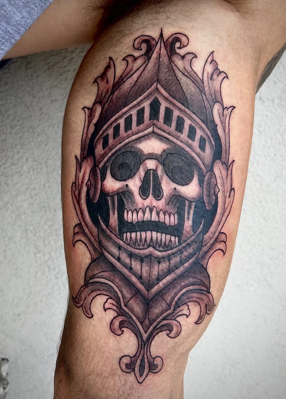 Black and grey illustrative skull in an ornate knight's helmet covers the inner upper arm.