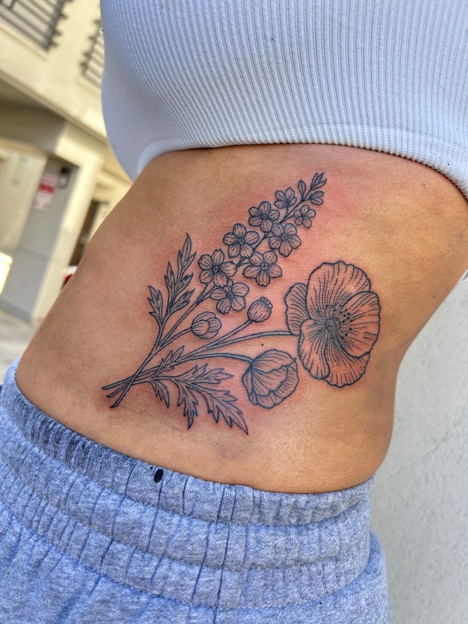 Black fine-line poppies and small blossoms with leafy stems sit on the side of the abdomen.