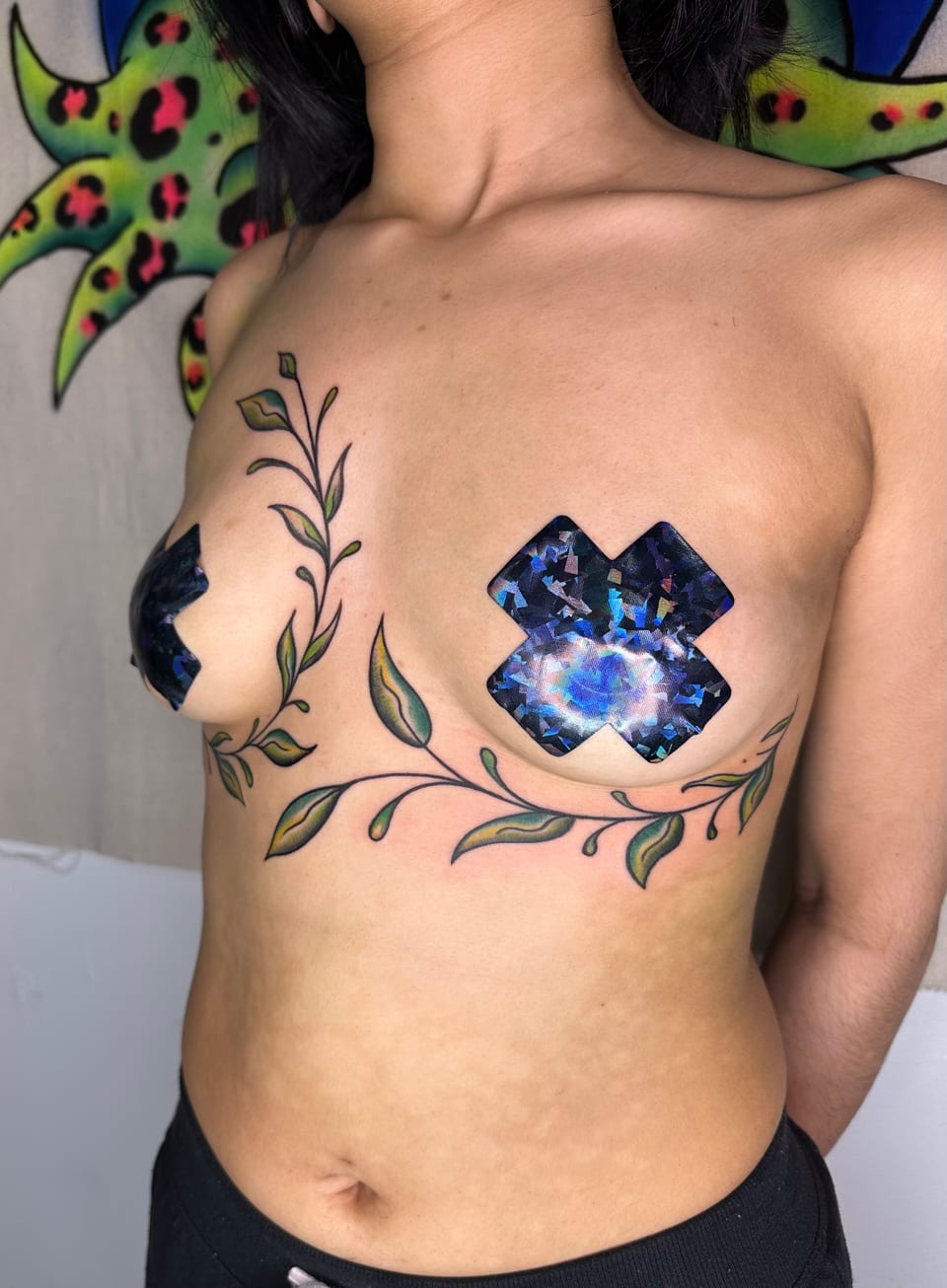 Leafy vine tattoos sweep beneath the chest in a side view.