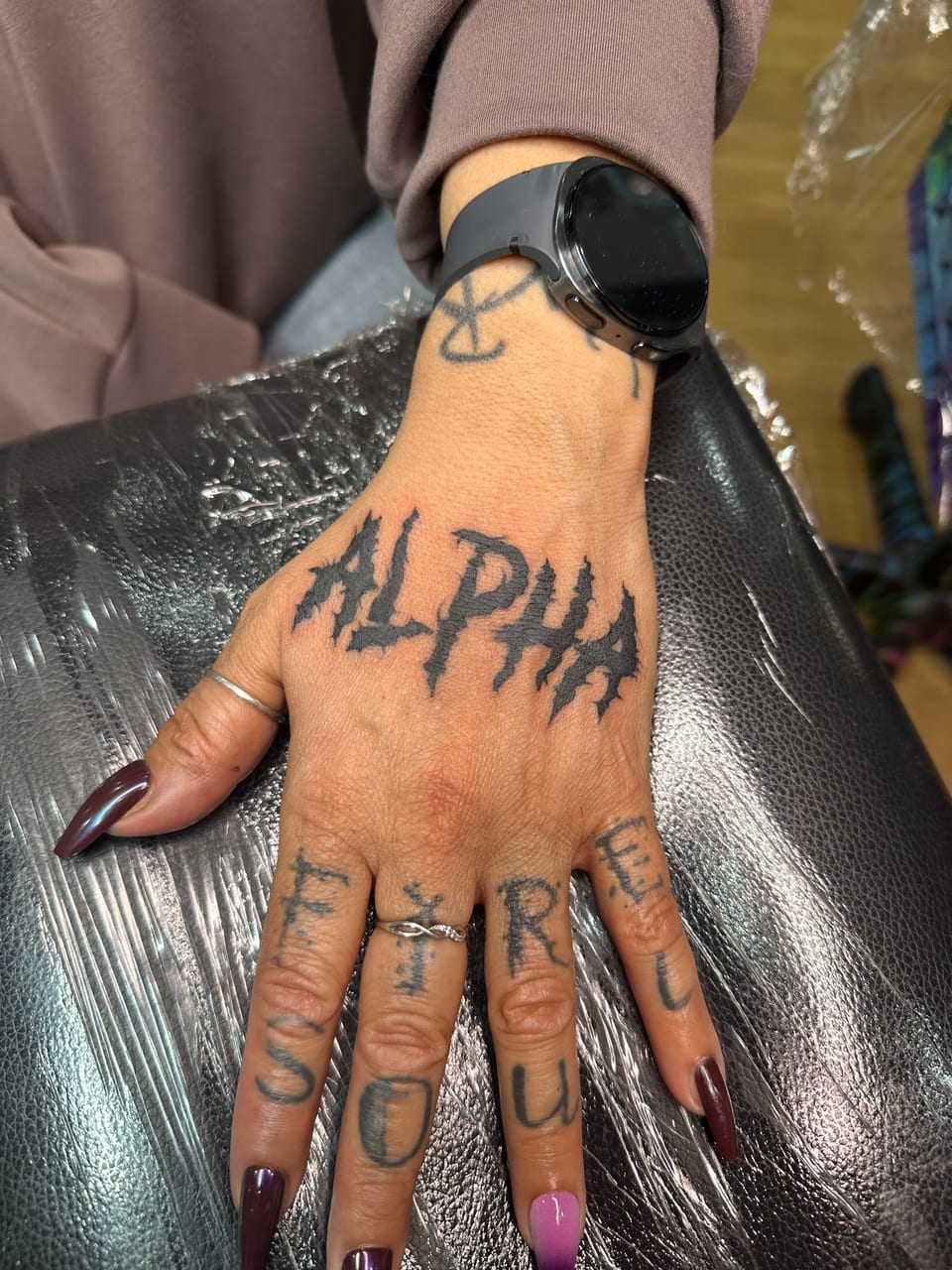 Jagged black ALPHA lettering stretches across the back of a hand.