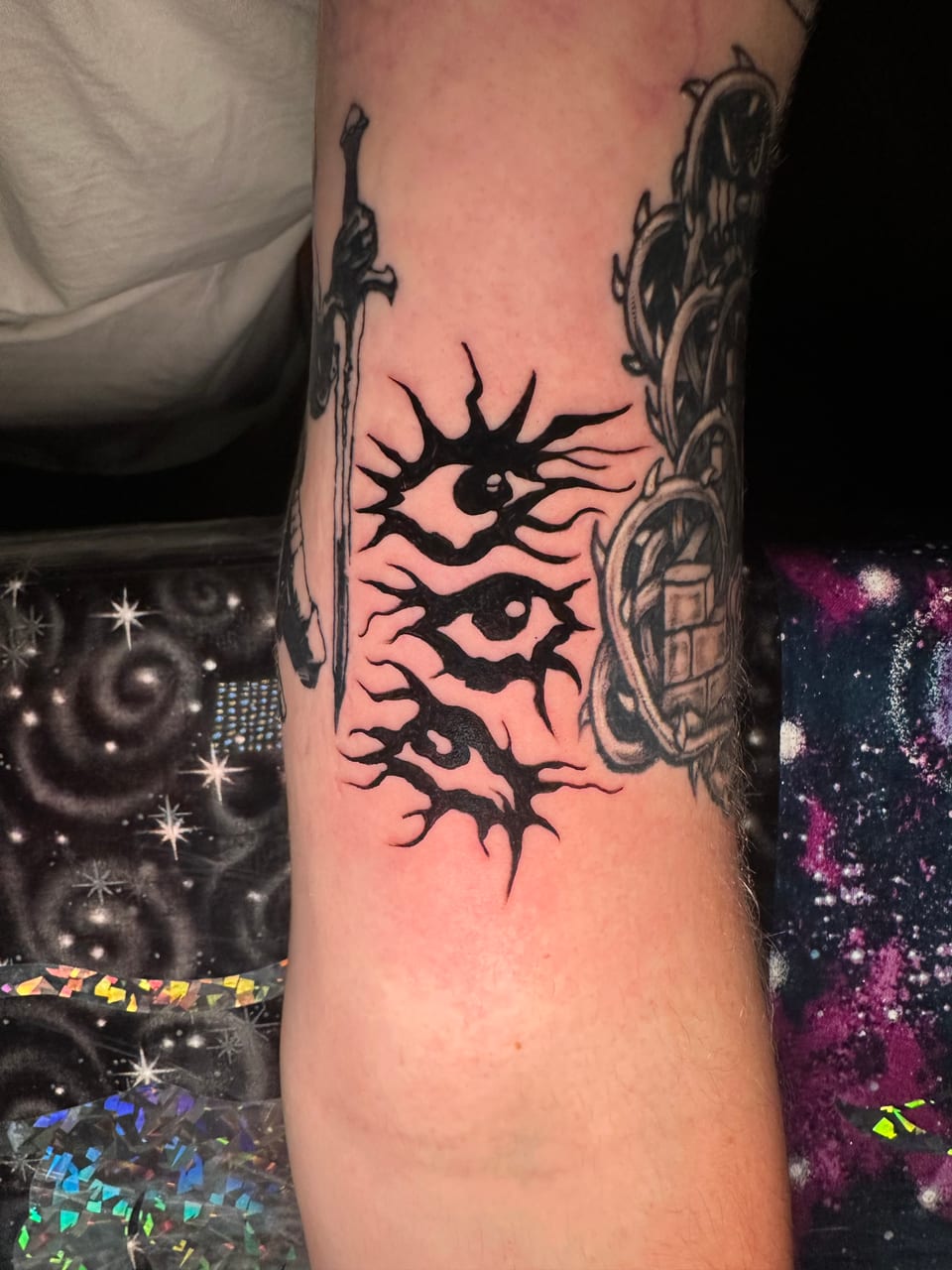 Stacked black eyes with spiked outlines fill a gap between forearm tattoos.