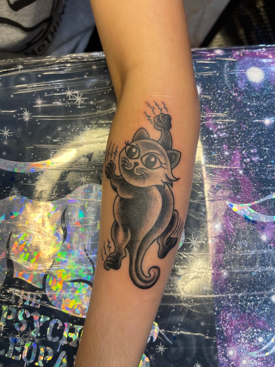 A black and grey cartoon cat tattoo stretches along a forearm.
