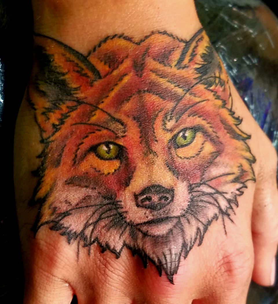 An orange fox face tattoo covers the back of a hand.