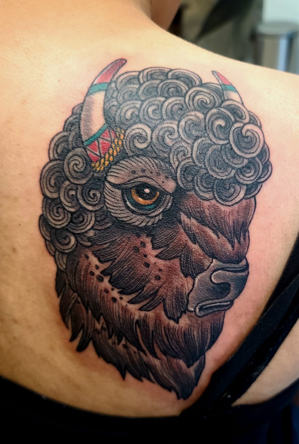 A bison head tattoo has curled fur and a single eye above its muzzle.