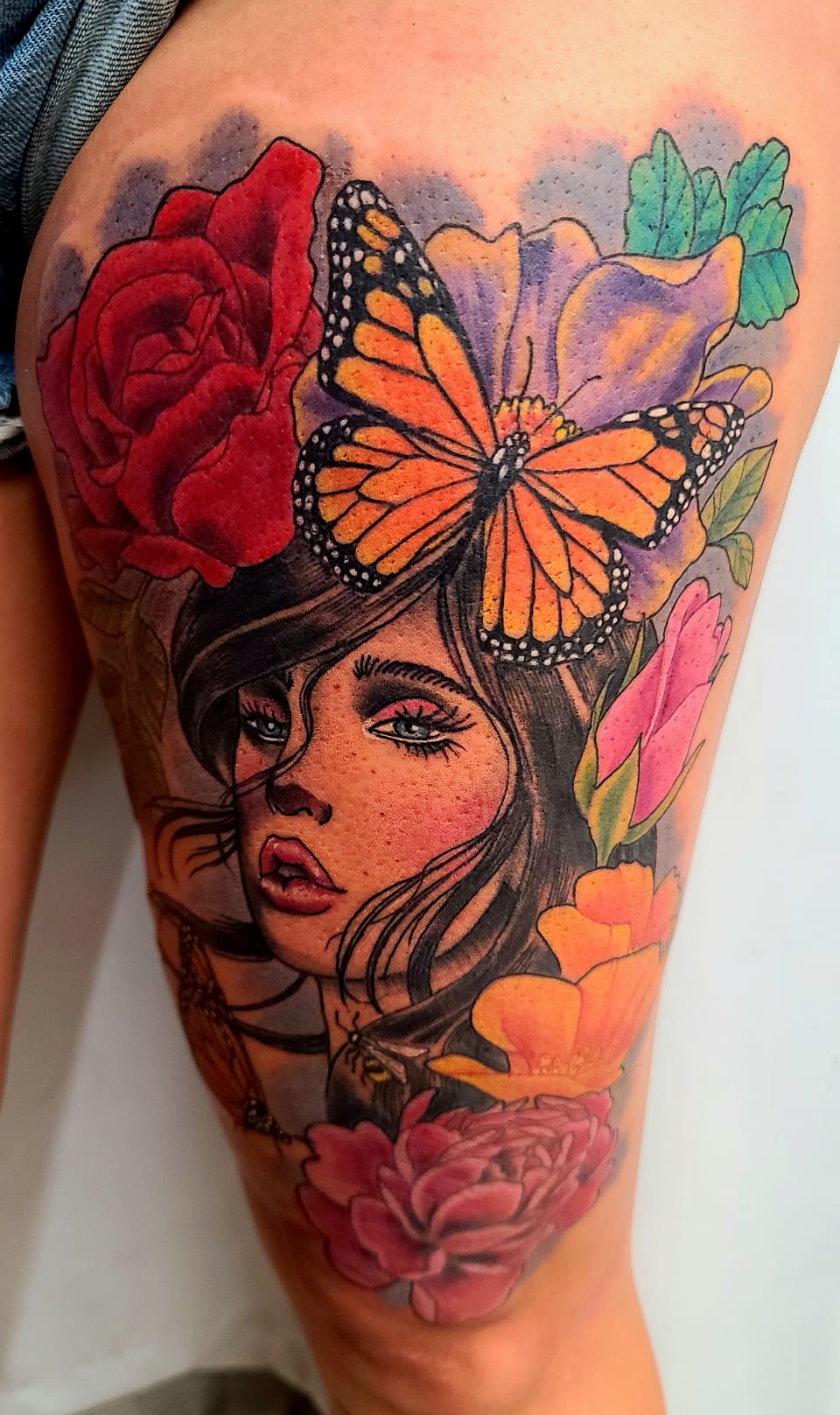 A woman with roses and an orange butterfly fills an upper-arm tattoo.
