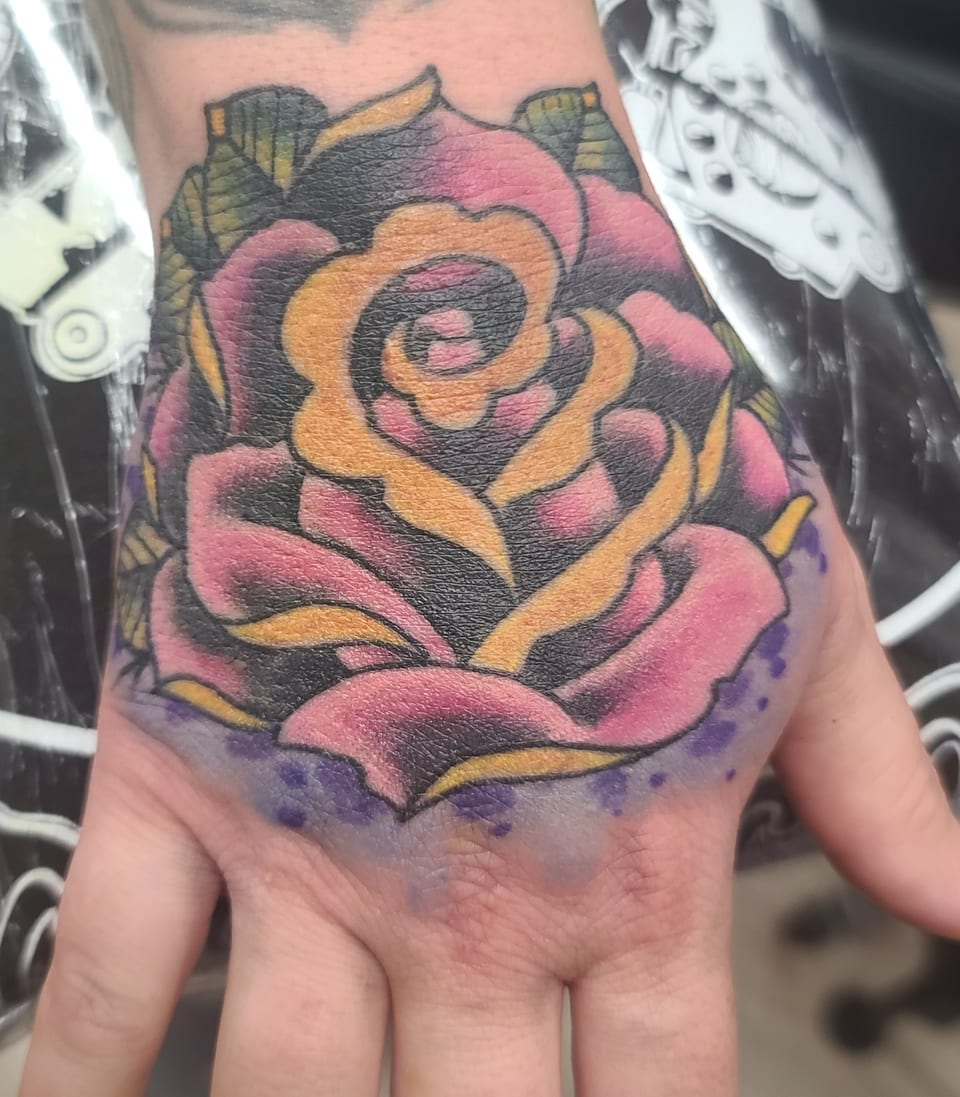 A pink and gold rose tattoo covers the back of a hand.