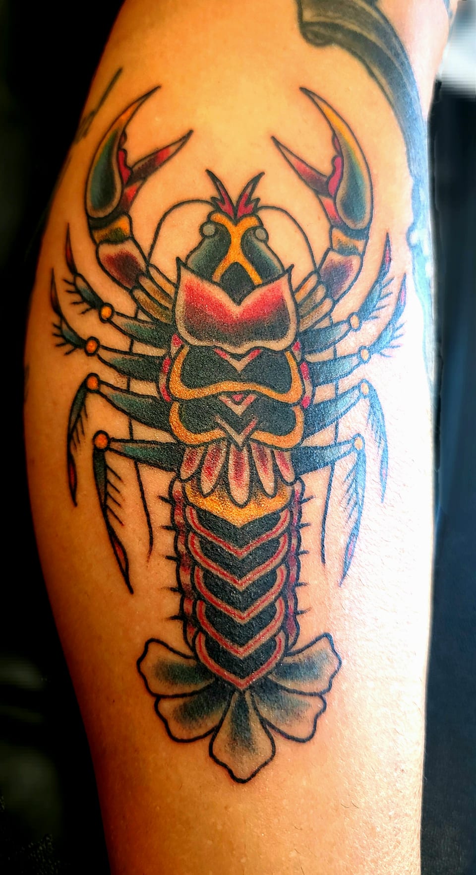 A red, gold and black scorpion tattoo stretches along an arm.