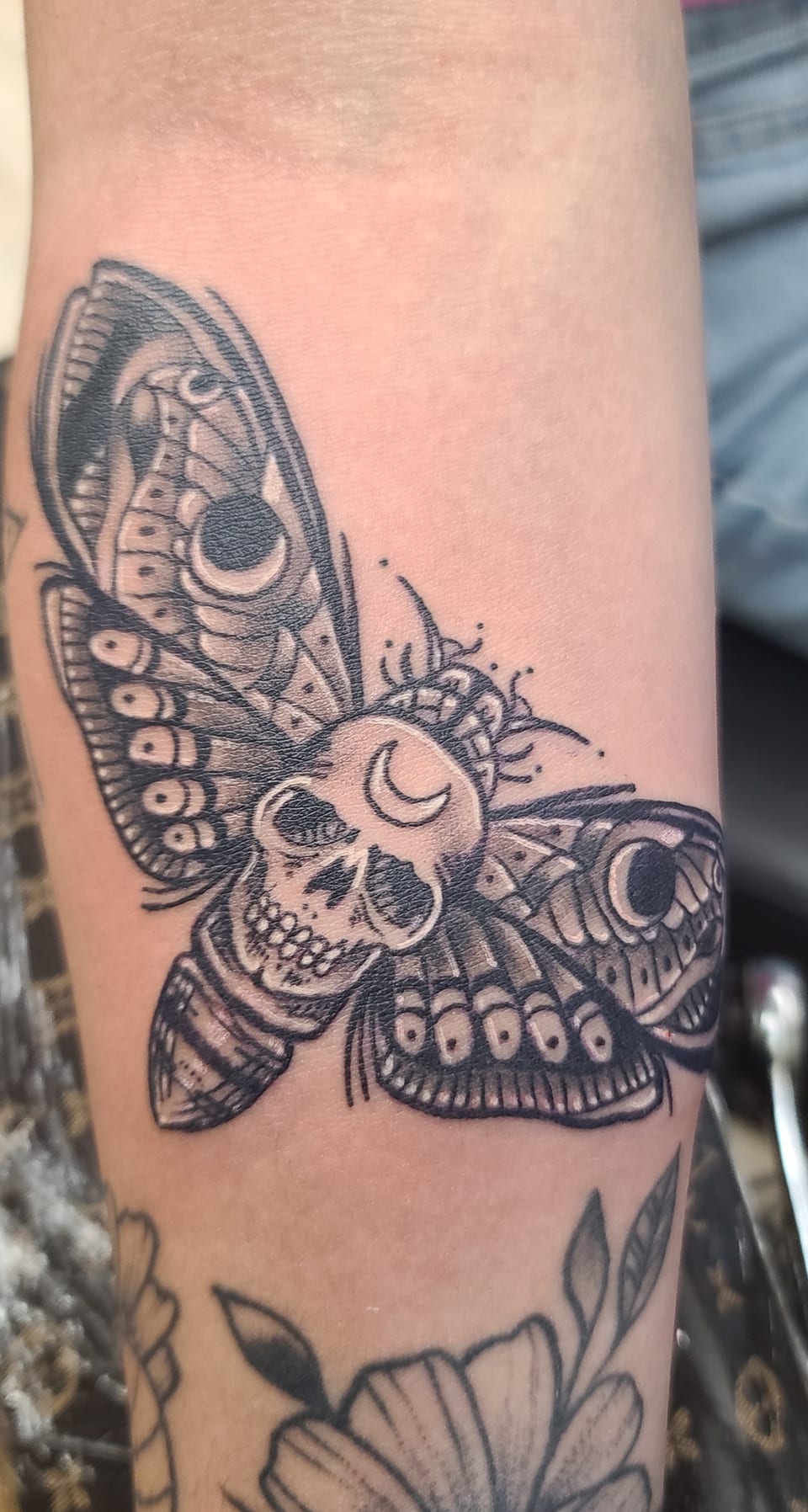 A black and grey moth tattoo has skull-like markings on its wings.