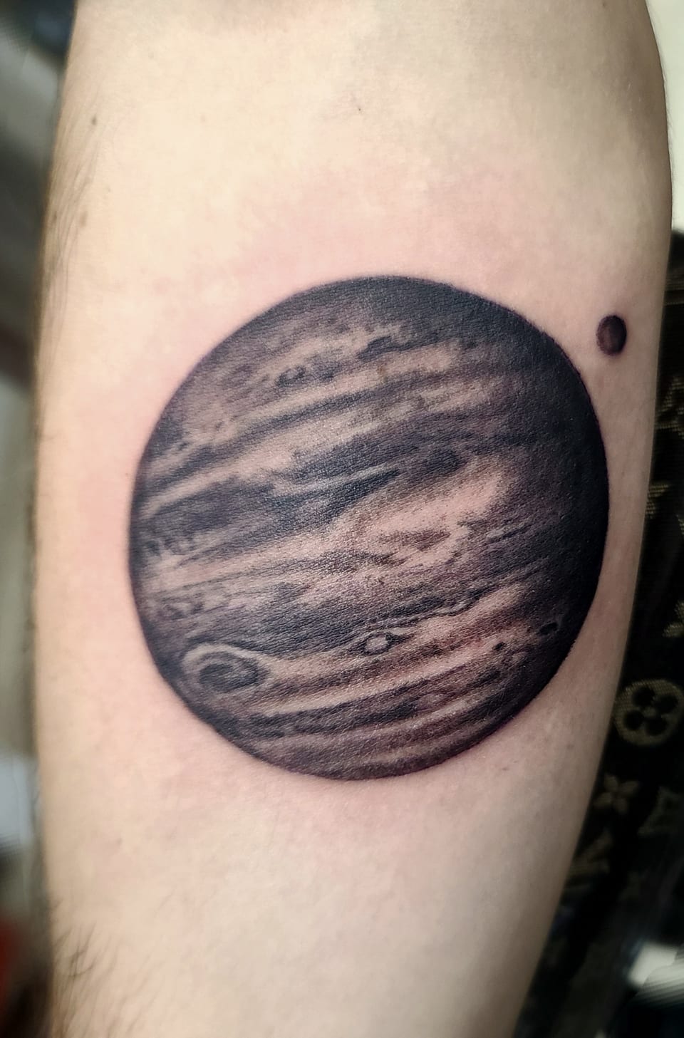 A shaded Jupiter tattoo has dark cloud bands and a small moon.