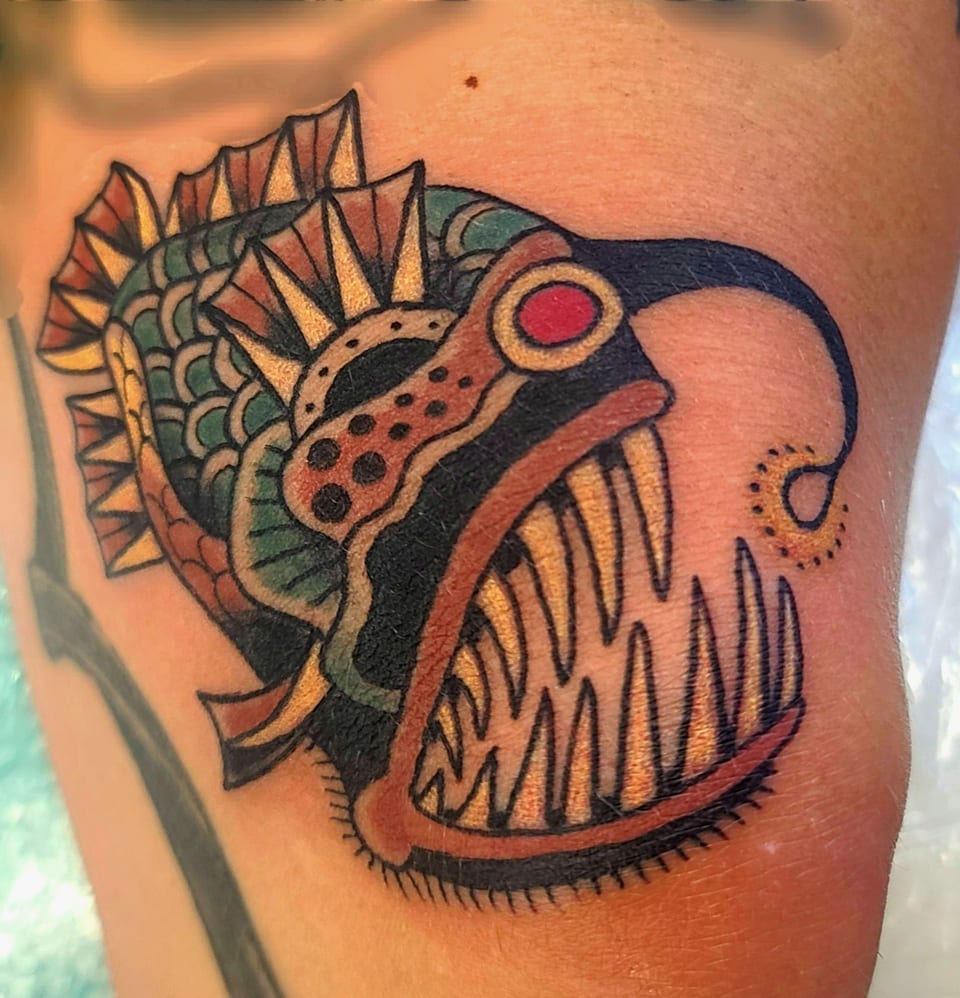 A colorful open-jawed creature tattoo has teeth, scales and red accents.