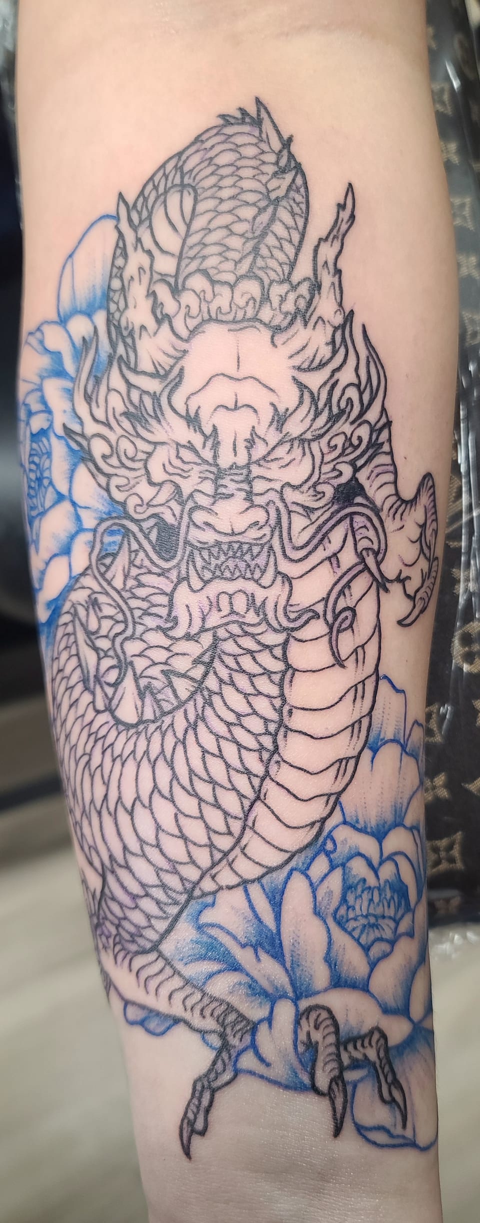 An outlined ornamental serpent tattoo curls among flowers along an arm.