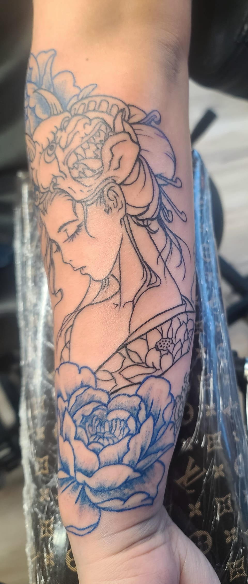 A woman in profile with an ornate floral headdress fills an arm tattoo.