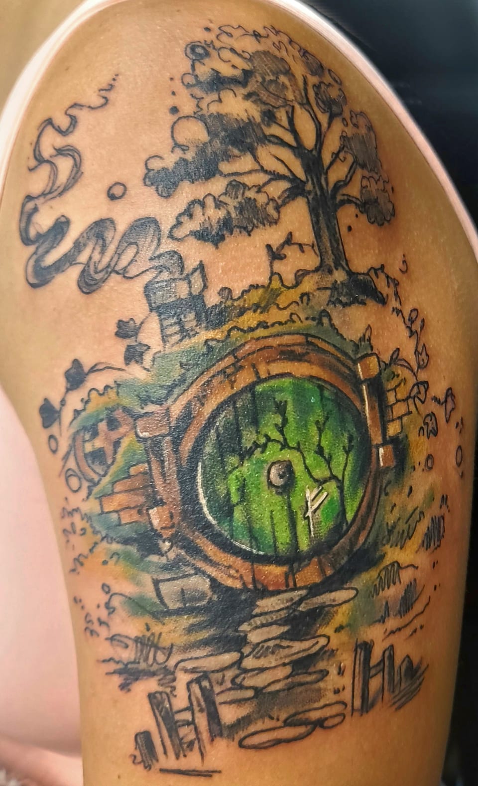 A green round doorway sits beneath a tree in a colorful landscape tattoo.