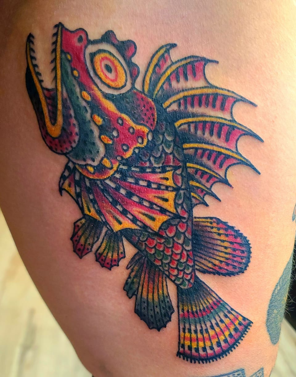A richly colored fish tattoo spreads patterned fins across an arm.